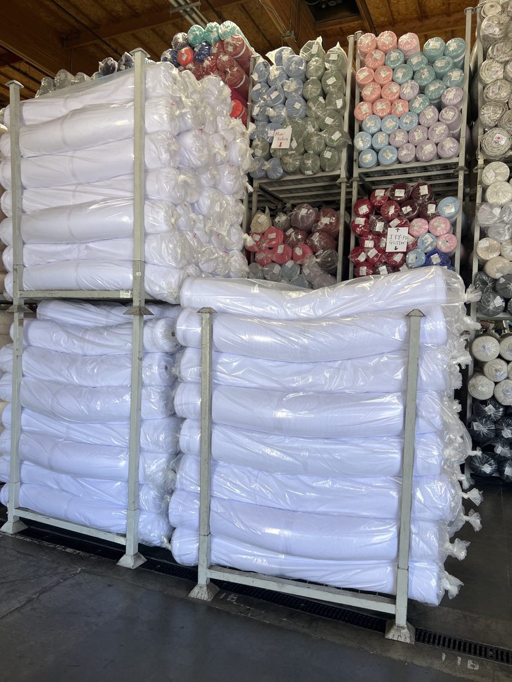 Fabric warehouse racks holding white polyester blanks alongside dyed colorways